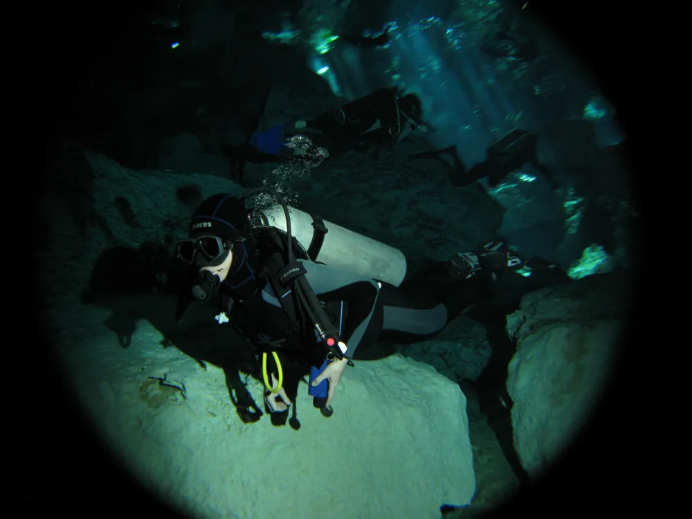 Die Autorin beim Höhlentauchen in einer Cenote, im Hintergrund Lichtstrahlen und andere Taucher als Schatten